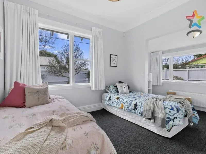 Bright bedroom with two twin beds, white curtains, and a large window