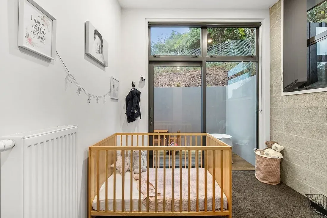 Modern nursery with wooden crib, white walls, window light, and stone fireplace trim