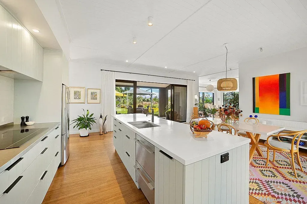 Bright modern kitchen and dining area with white island, wood floor, colorful wall art, and hanging lights