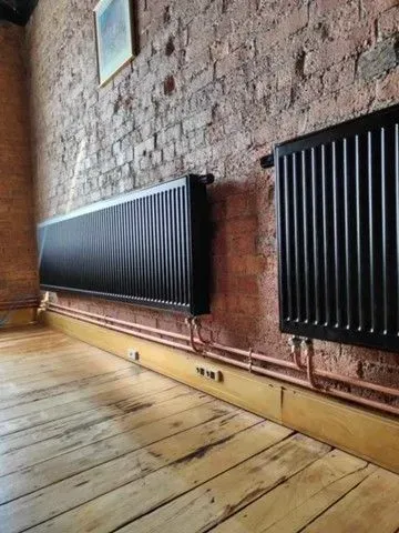 Brick-walled room with black radiators along the wall and a wooden floor
