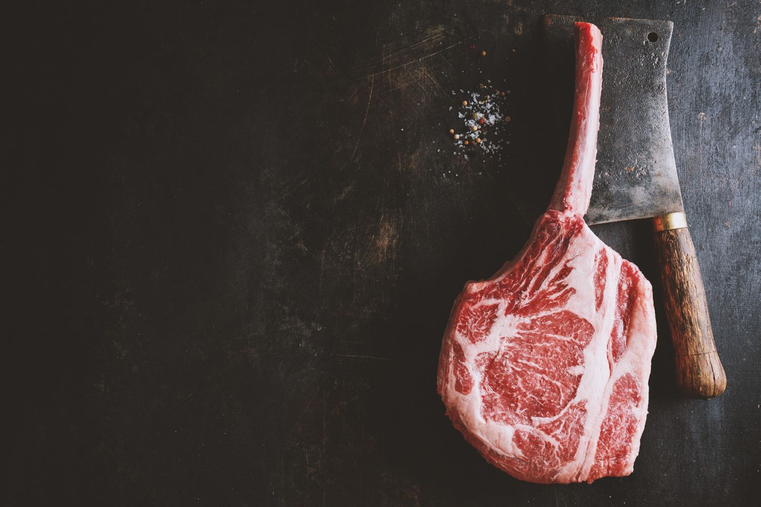 Bistecca cruda marmorizzata con un rametto di rosmarino accanto a un coltello su una superficie scura