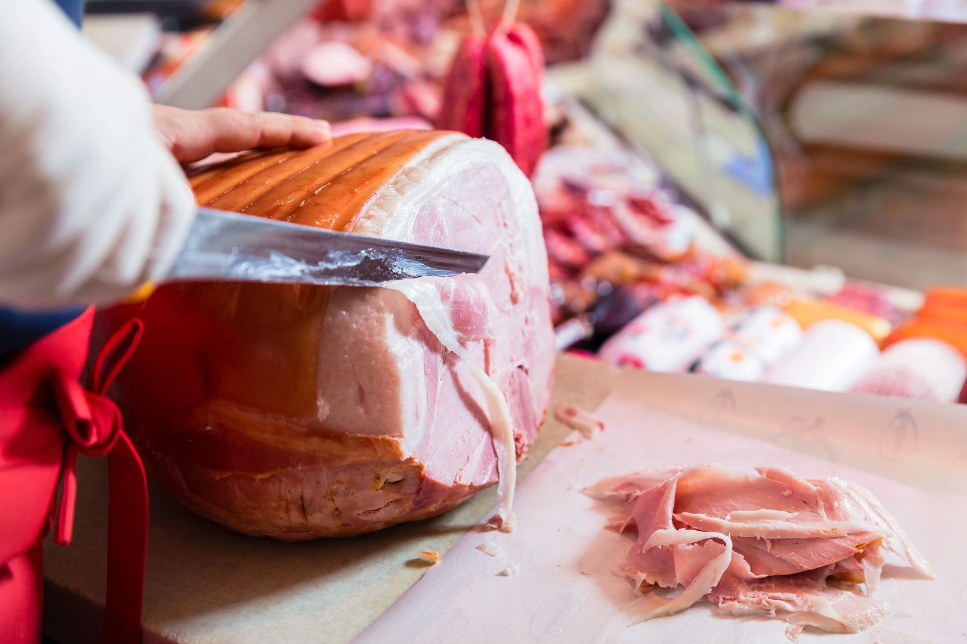Una persona affetta a mano un grosso prosciutto su un tagliere, con le fette ammucchiate accanto.