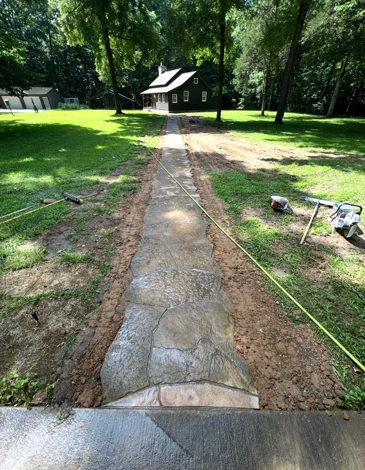 Stone walkway leading through a grassy park to a small pavilion surrounded by trees