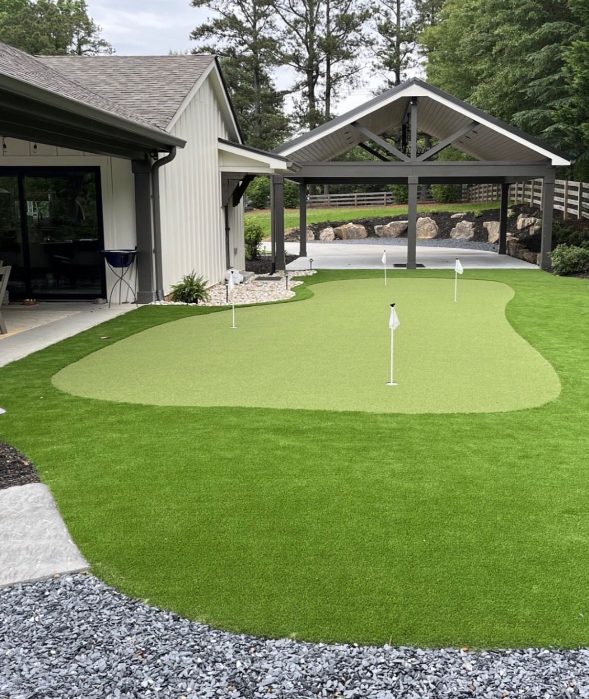 Small artificial putting green with a white flag and cup, bordered by concrete walls and walkway