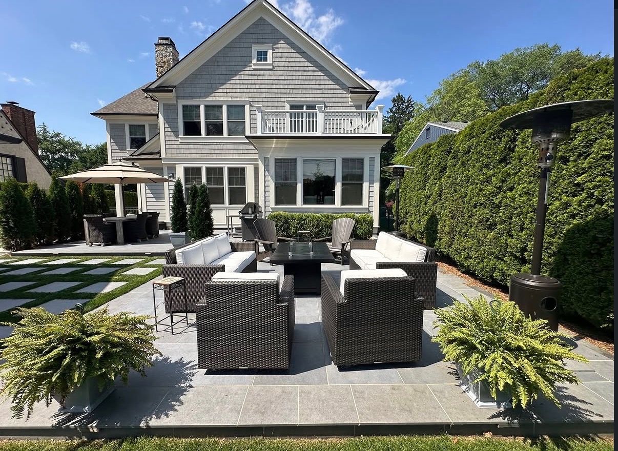 Modern house with a sunlit patio, wicker seating, and lush greenery in the backyard