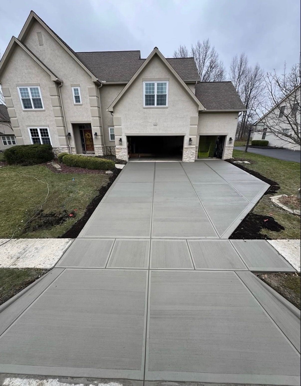 Concrete driveway leading to a beige house with a two-car garage on a cloudy day