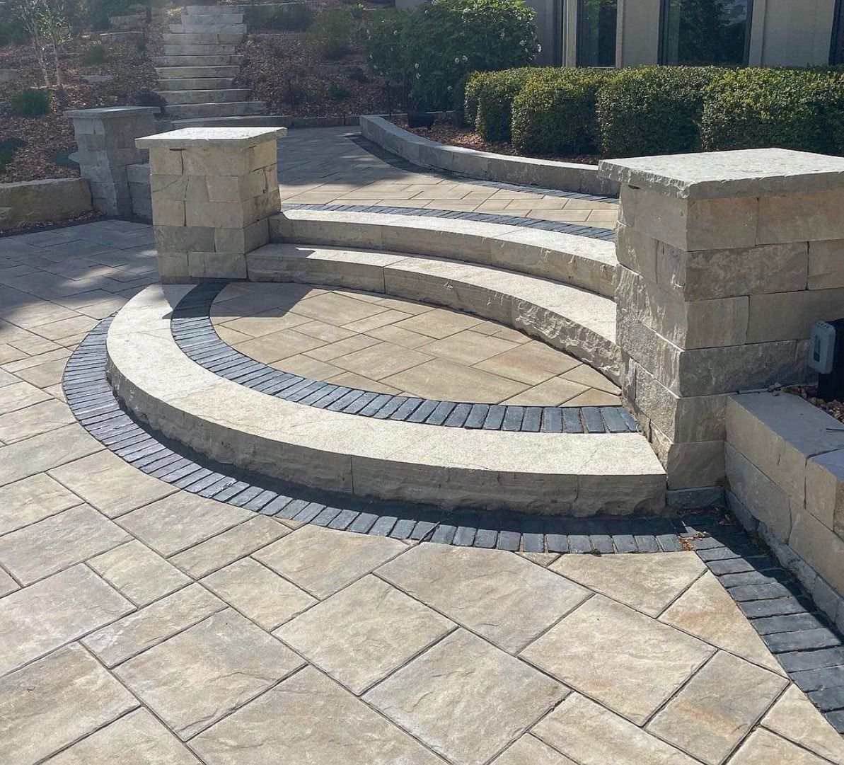 Curved stone steps and circular patio paving beside a landscaped outdoor walkway