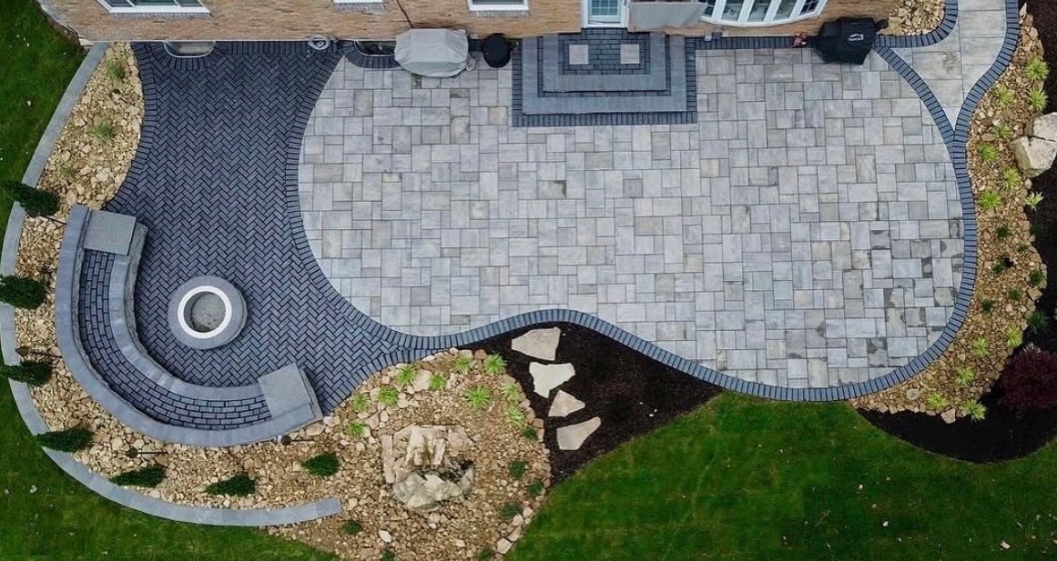 Curved stone patio and walkway beside a green lawn and landscaped garden border.