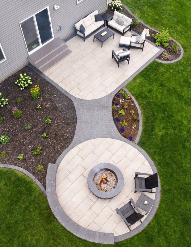 Aerial view of a backyard patio with outdoor seating and a circular fire pit area surrounded by landscaping.