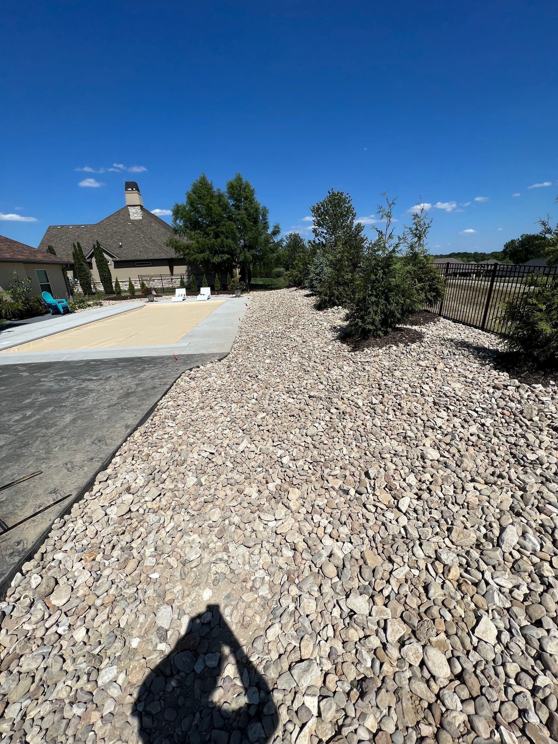 Rock-covered landscaping beside a driveway and house under a clear blue sky