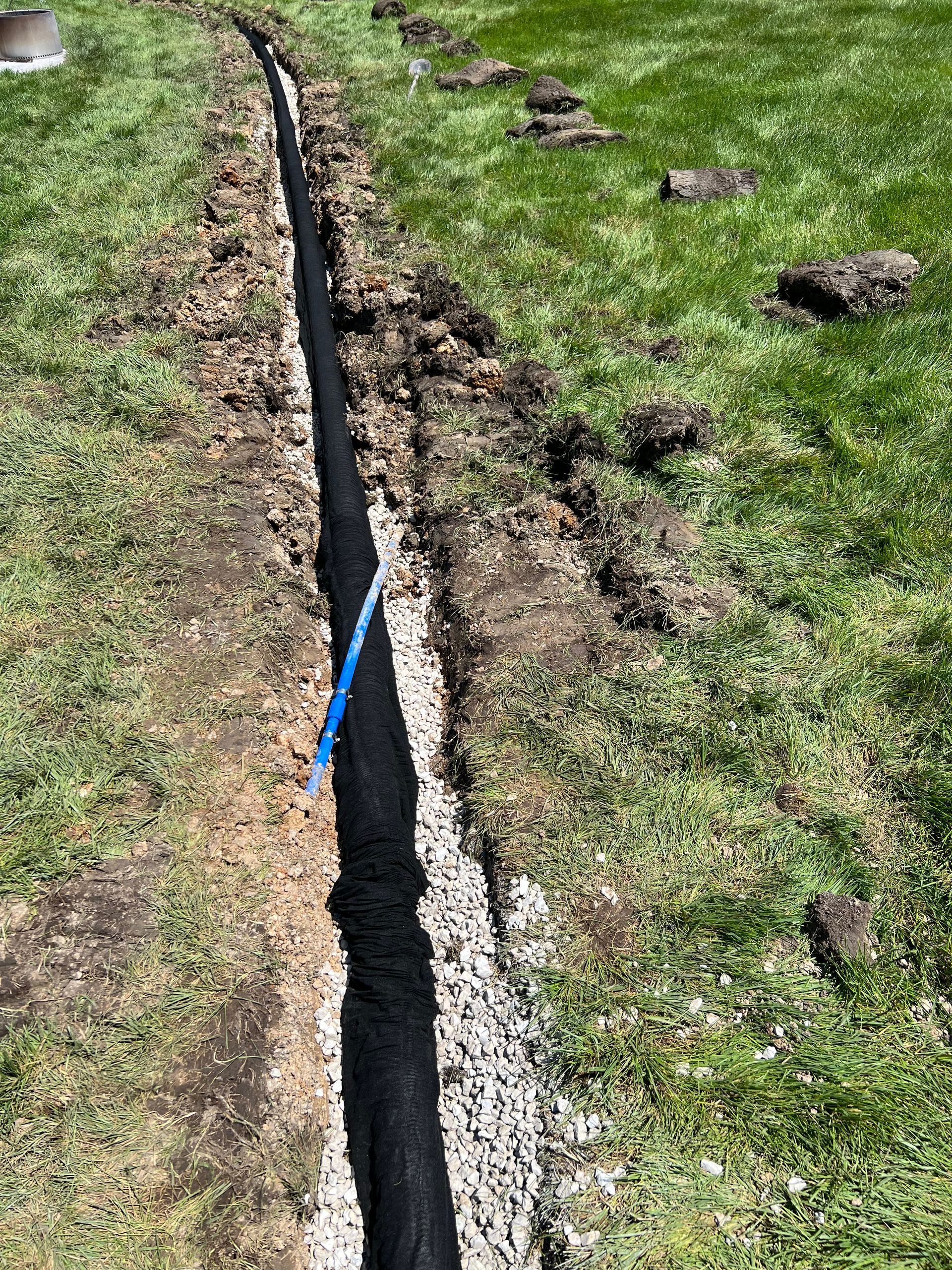 A long cracked trench in a grassy field with a blue pipe or cable running through it.