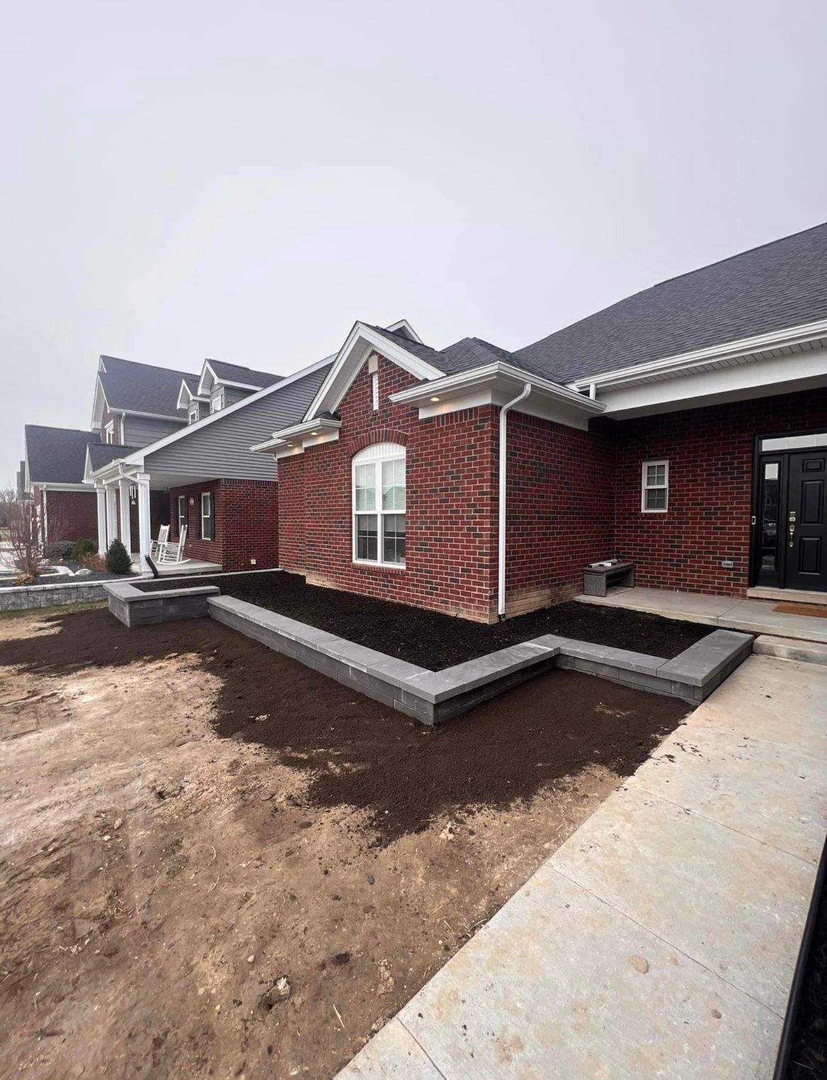 Brick house exterior with unfinished yard and concrete walkway under overcast sky