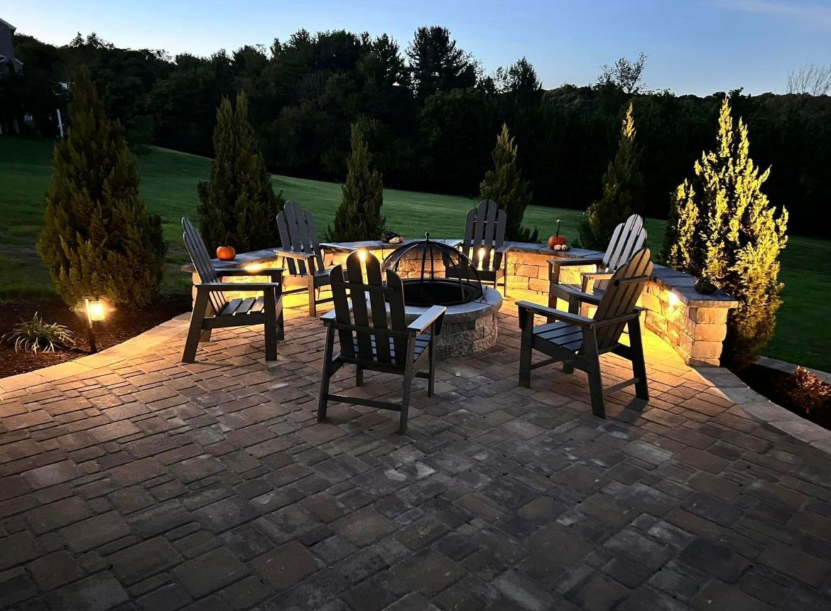 Outdoor patio with fire pit, black chairs, and string lights at dusk, surrounded by trees