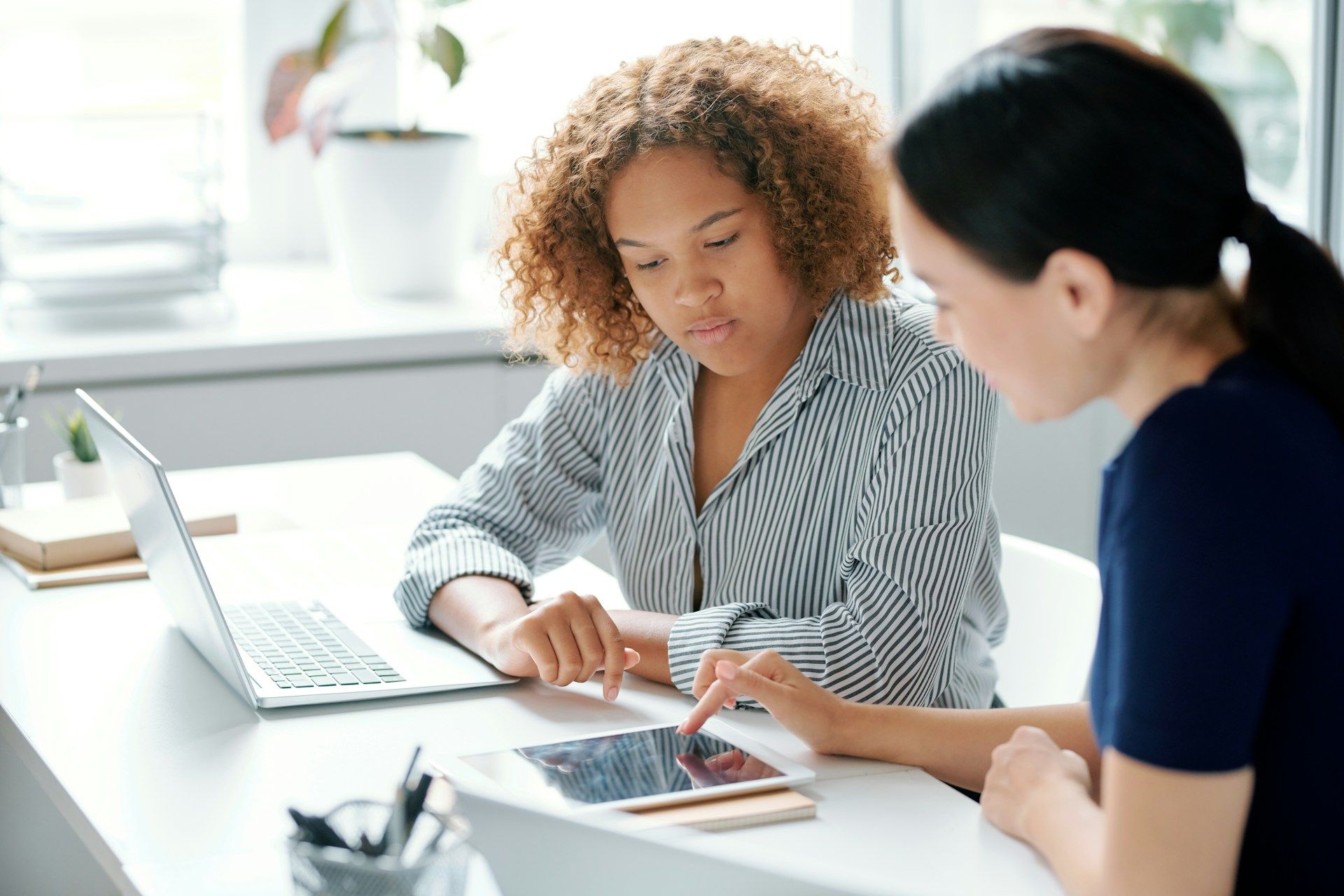 Two people at a desk reviewing a tablet. One points to the screen; both appear focused.