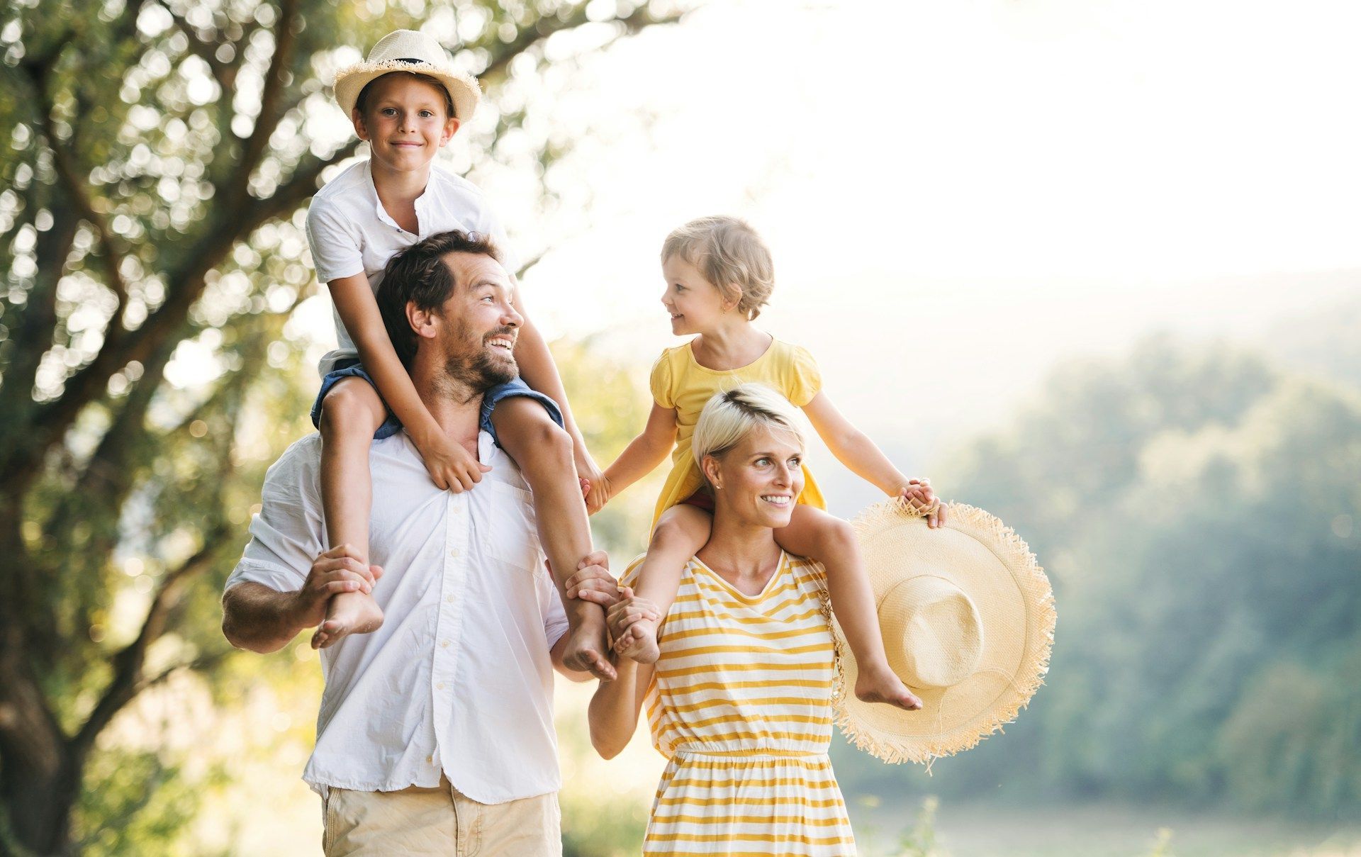 Family with two children on their shoulders smiling outside.