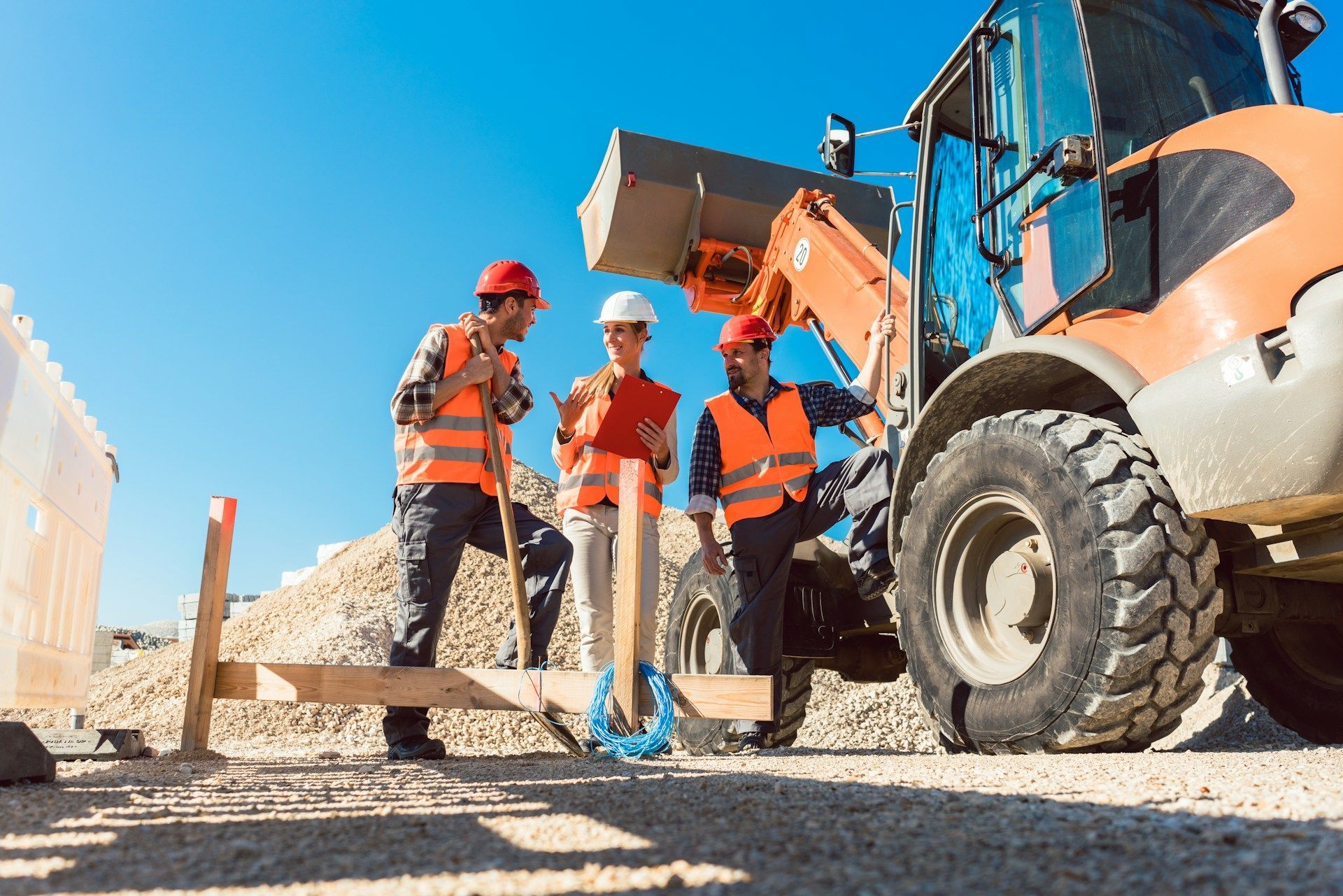 Construction workers with safety vests discussing plans near an excavator on a sunny day.