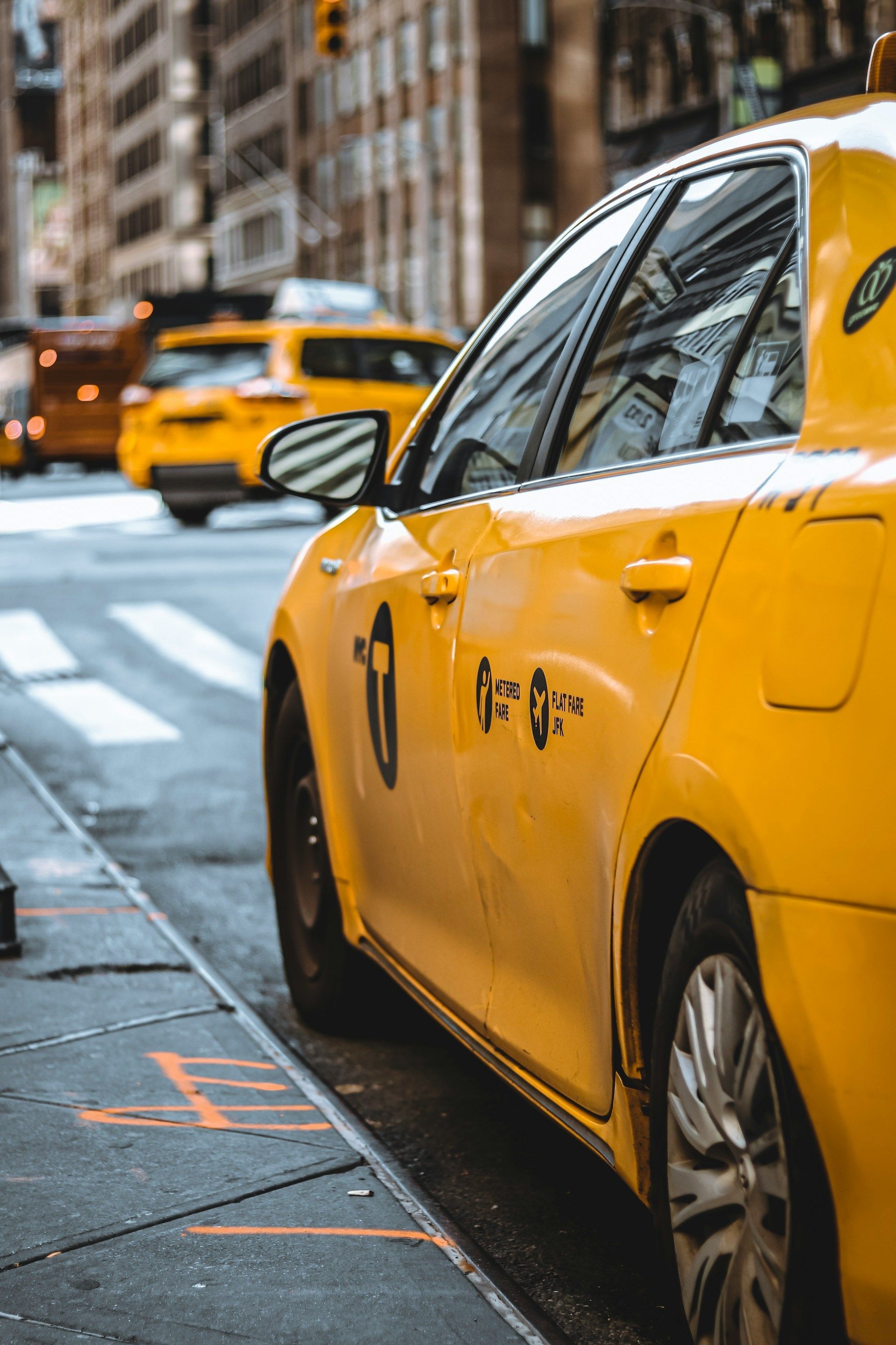 Yellow taxi cab parked on a city street, another taxi in the background.