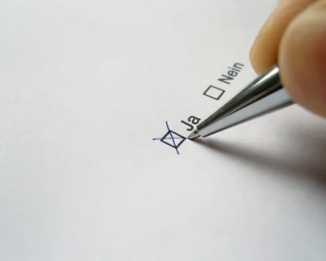 Eine Person markiert mit einem Stift ein Kästchen mit der Aufschrift „Ja“