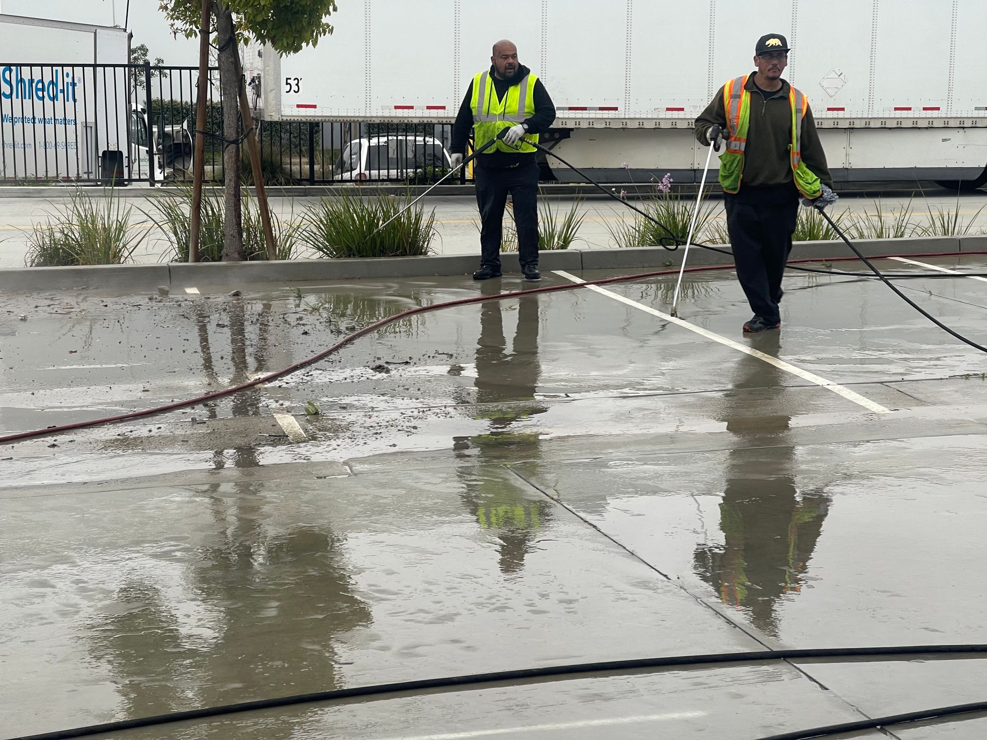 Two men are cleaning a parking lot in the rain.