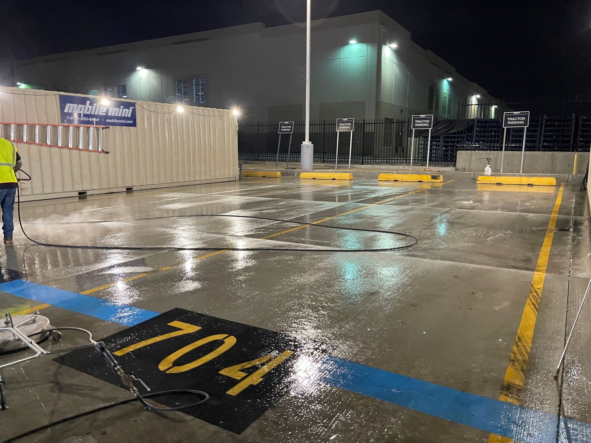 A man is cleaning a parking lot at night with a high pressure washer.