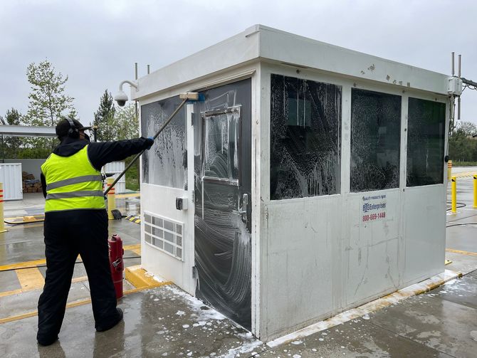 A man in a yellow vest is cleaning a building with a broom.