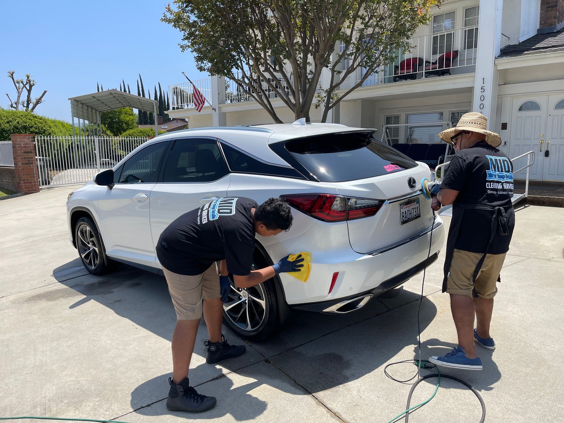 Two men are washing a white car in a driveway.