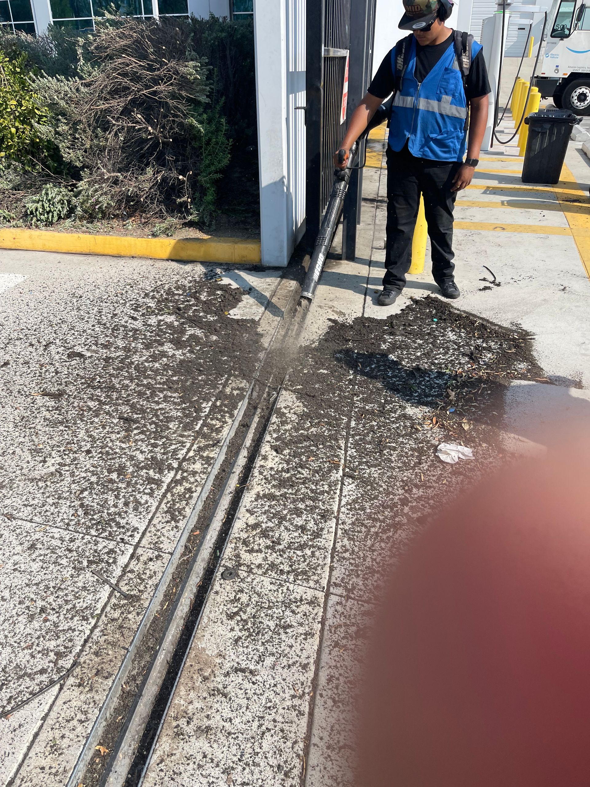 A man in a blue vest is cleaning a sidewalk with a shovel.