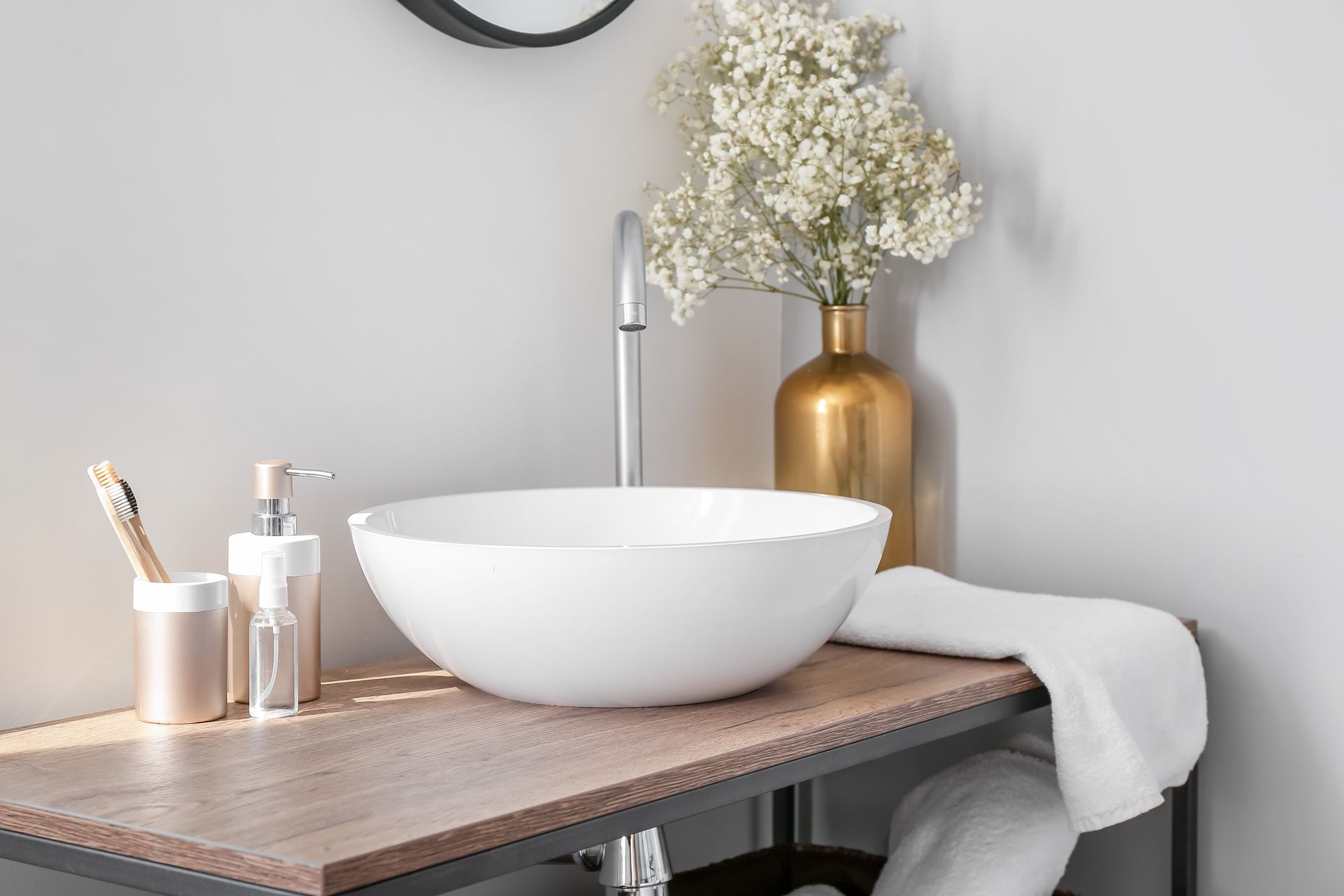 Une salle de bain avec un lavabo, un miroir, des brosses à dents et un vase de fleurs.