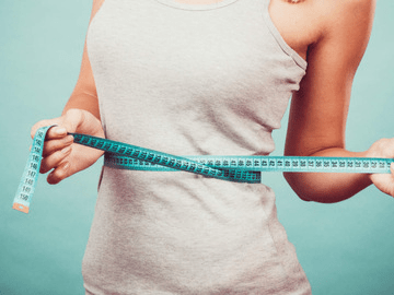 A woman is measuring her waist with a tape measure.