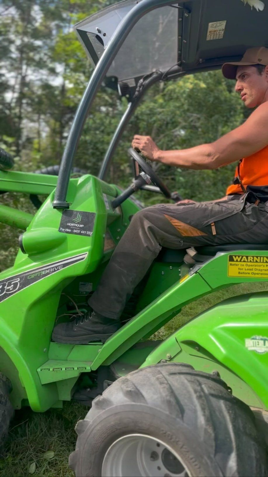 A Man Is Driving a Green Tractor in The Woods — Hinterland Tree & Stump Removal in Palmview, QLD