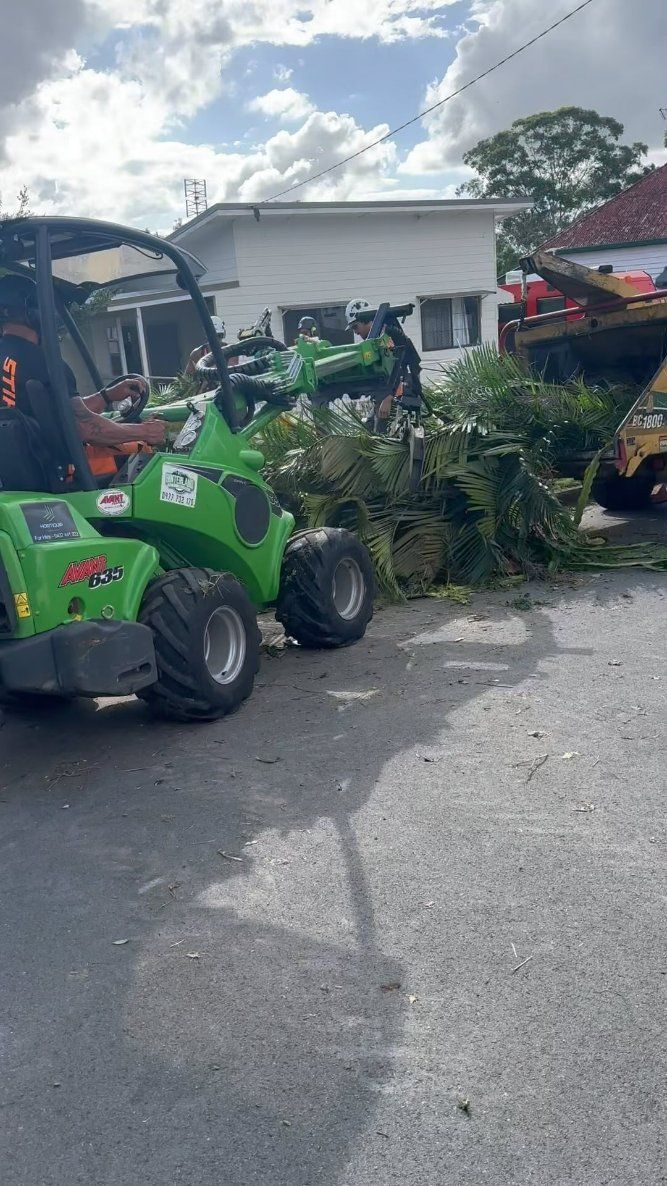 A Man Is Driving a Green Tractor Down a Street — Hinterland Tree & Stump Removal in Montville, QLD
