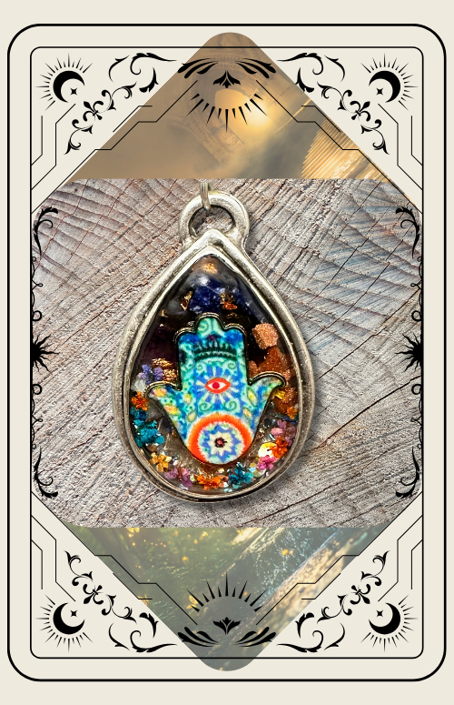 A teardrop-shaped pendant featuring a colorful Hamsa charm set in resin, framed by an ornate, occult-themed border.