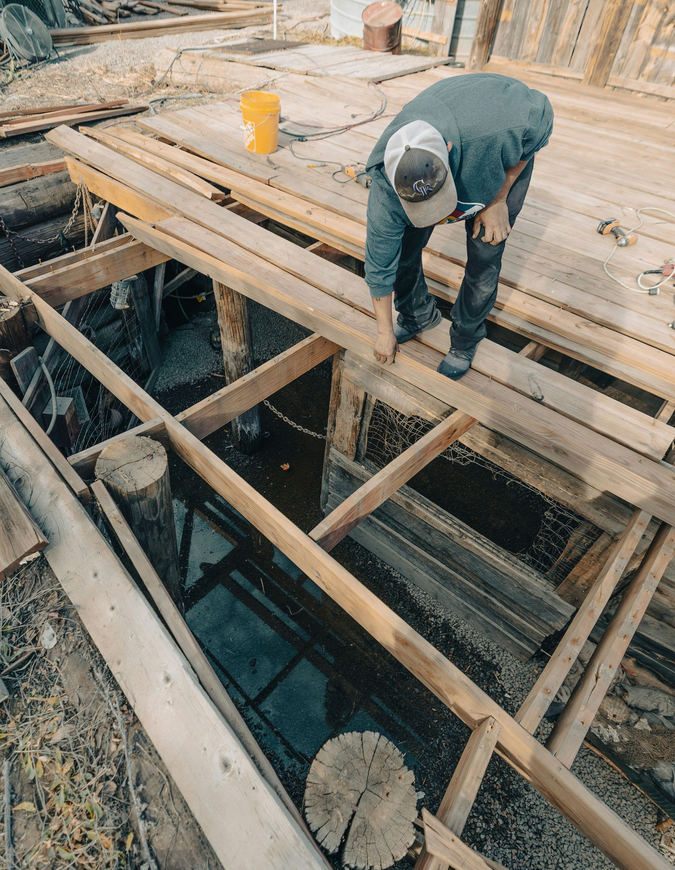 Worker bending over wooden beams at a construction site with an open framework below