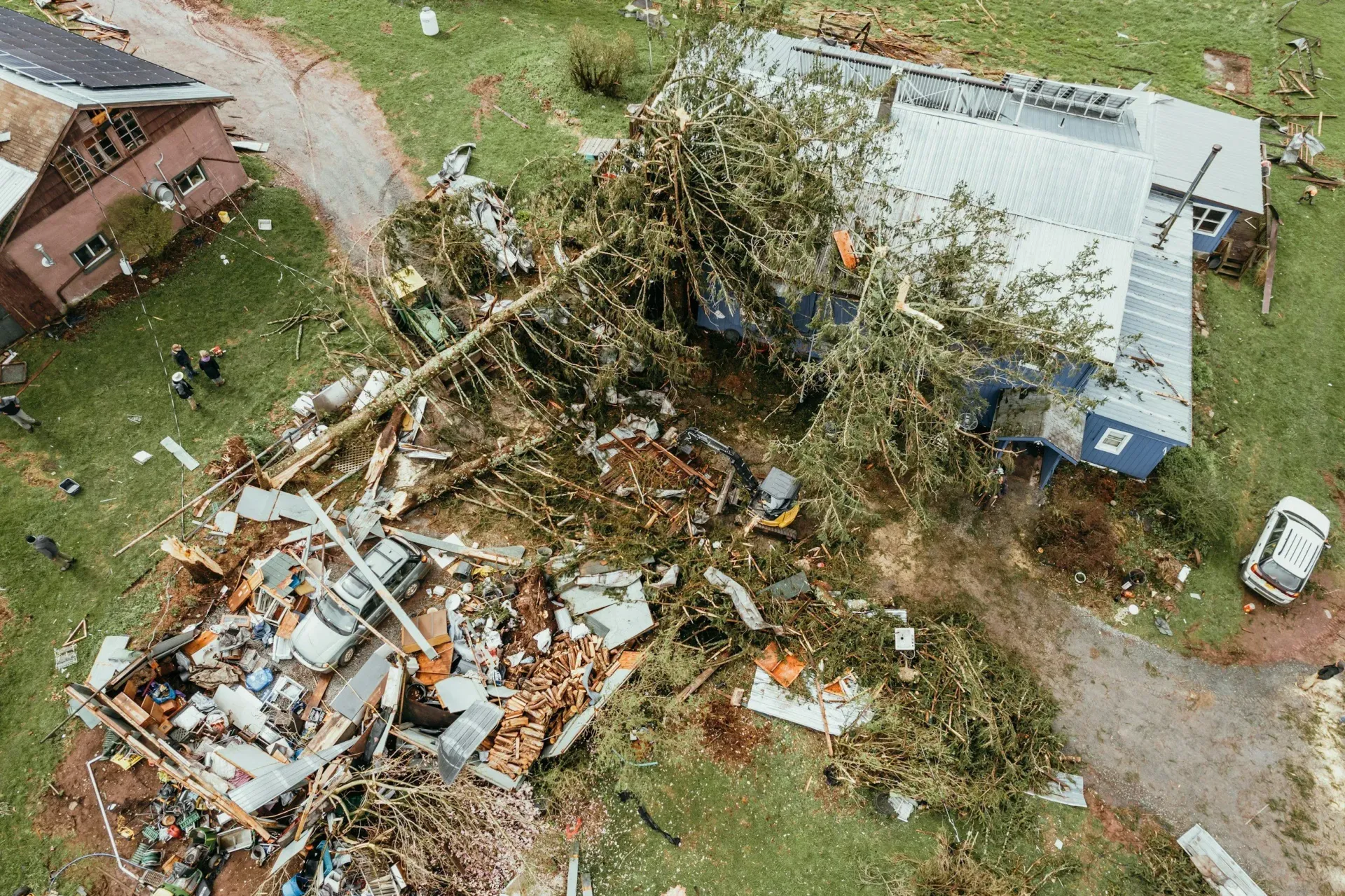 Aerial view of storm damage with debris, fallen trees, and damaged buildings along a dirt road