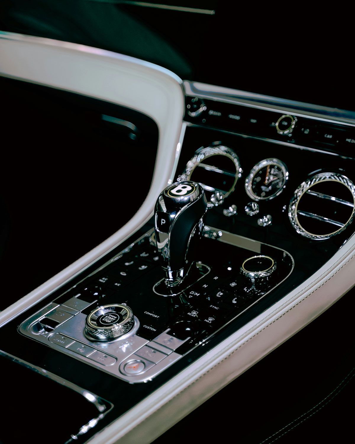 Bentley car interior, showing gear shift and dashboard controls. Black and chrome details with white trim.