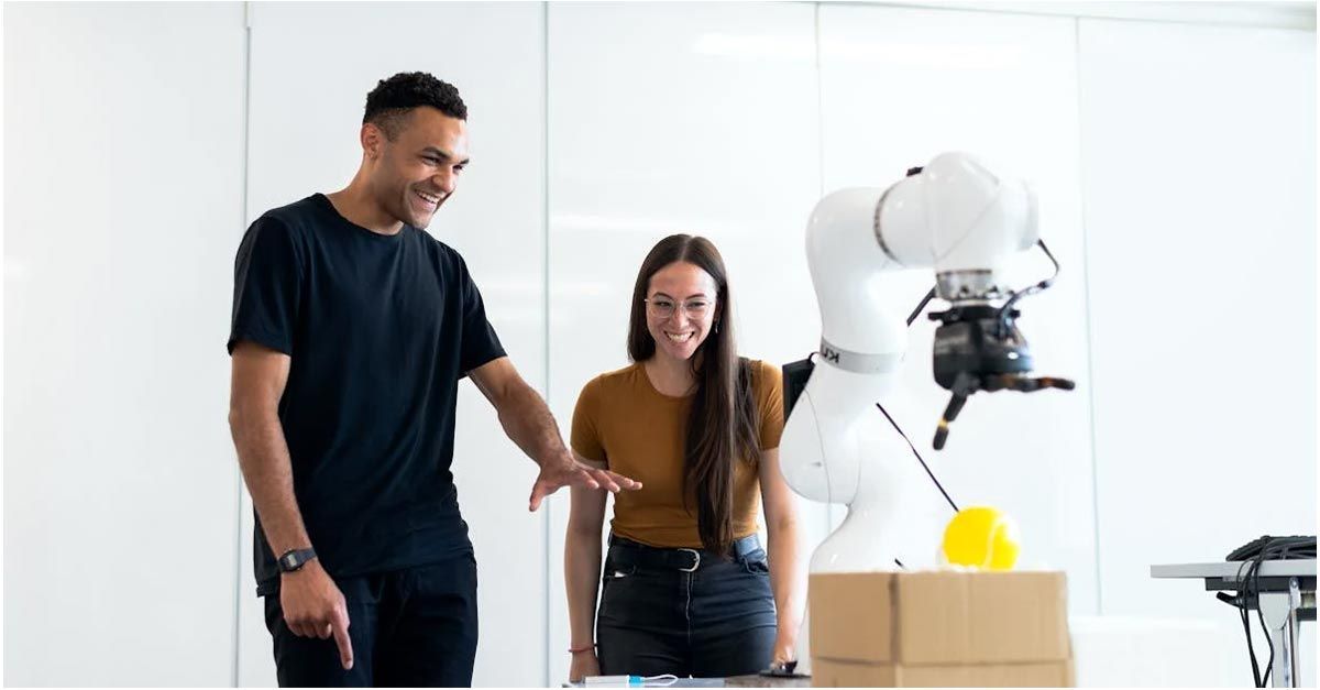 A man and a woman are standing next to a robotic arm.