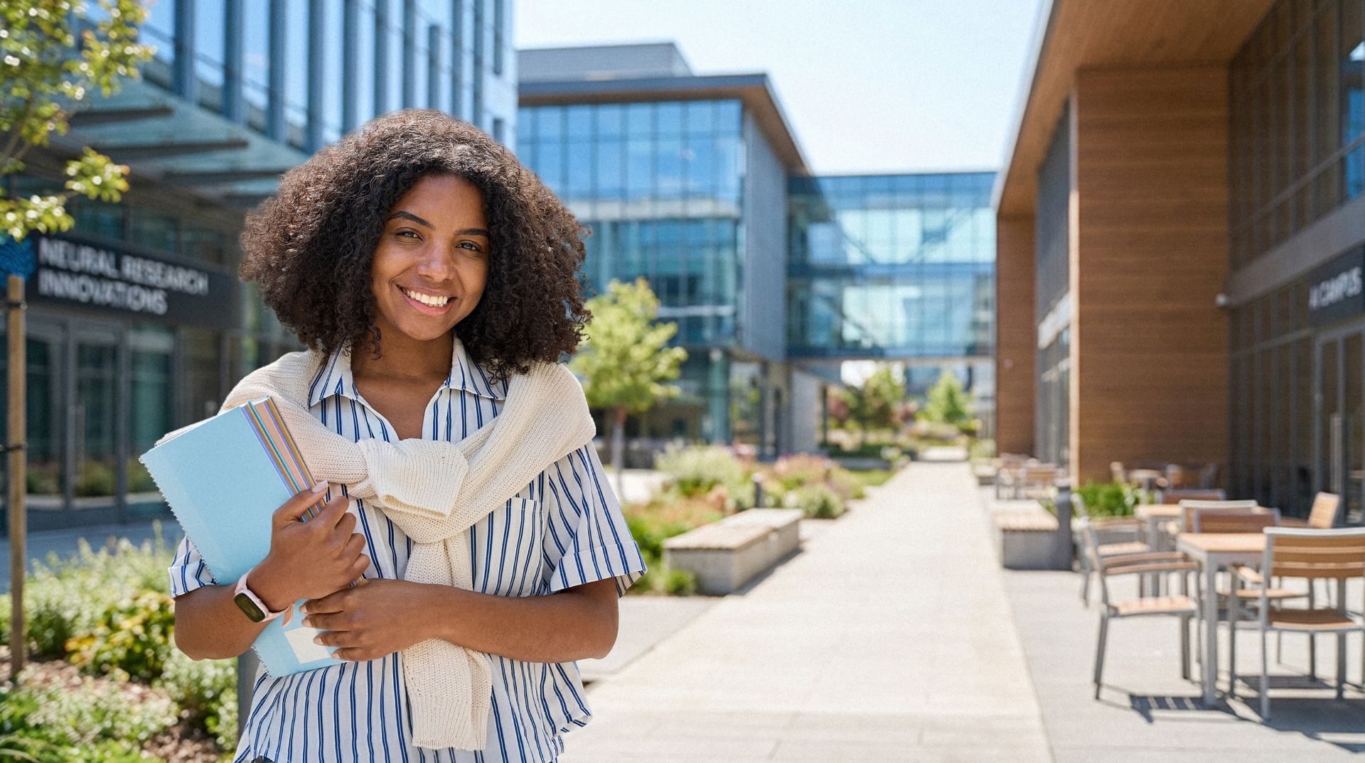 Smiling student holding books outside a modern campus building