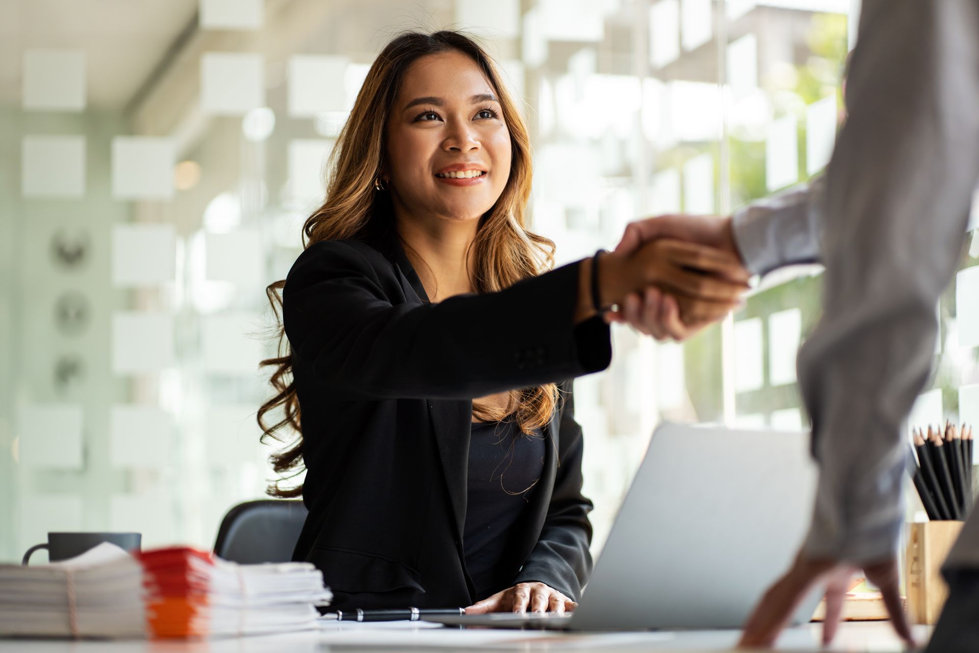 Businesswoman smiling and shaking hands across a desk in a bright office