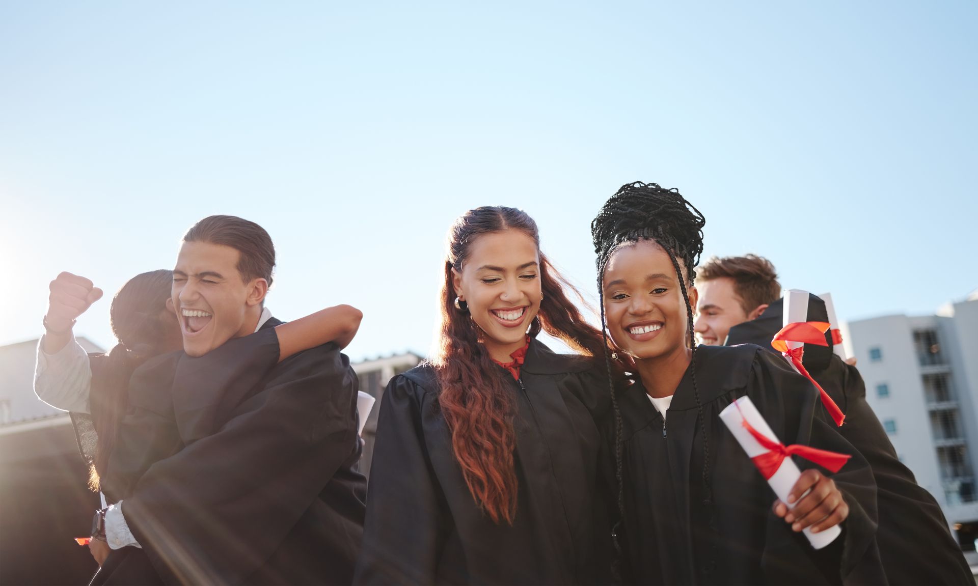 Three friends smiling and celebrating outdoors, holding flags in a sunny city setting