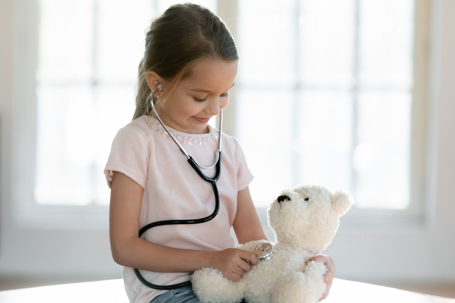 Little girl holding stethoscope to teddy bear's chest.