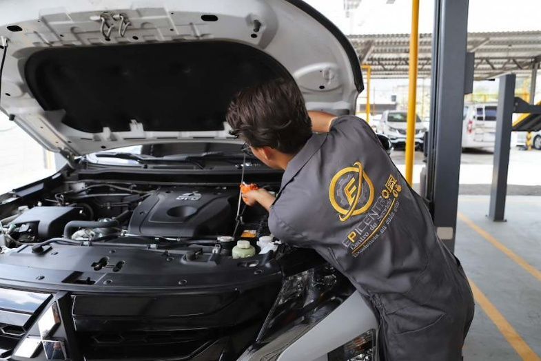Mecánico con mono azul trabajando bajo el capó de un coche en un taller de reparación de automóviles.
