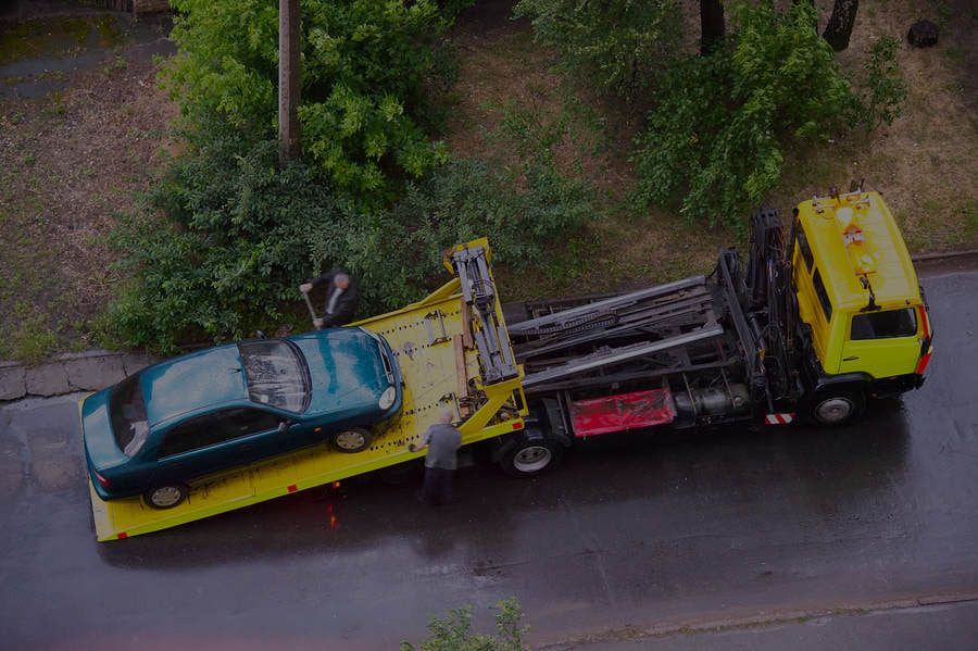 A tow truck is carrying a green car on a flatbed.