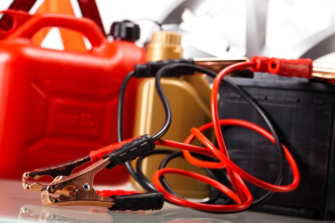 A red gas can , a battery , a jump starter , and a fuel can are on a table.