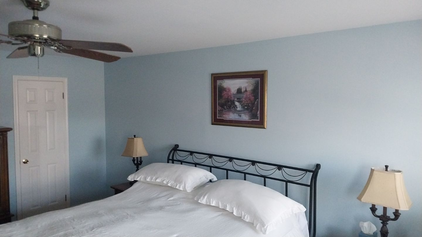 Freshly painted master bedroom with light blue walls, white ceiling, and white bathroom door – after interior painting project in Hatfield, PA.
