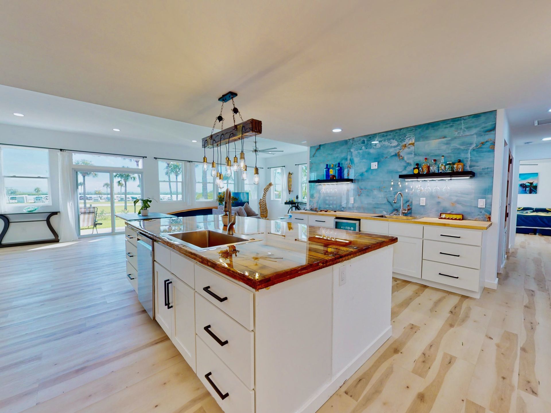 Bright kitchen with a large island, white cabinets, wood-look flooring, and a blue backsplash under a rustic light fixture.