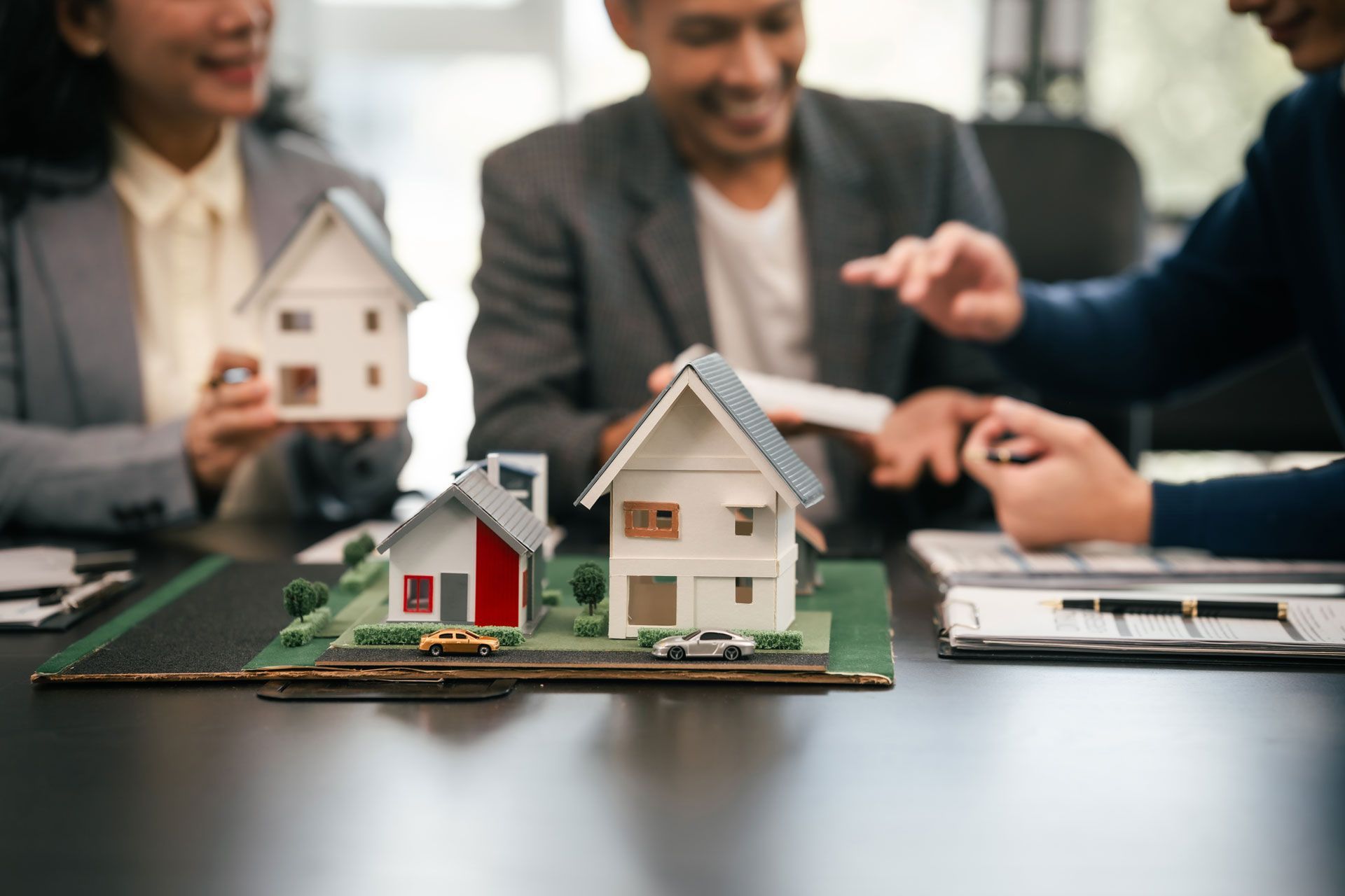 People sitting around a table with architectural house models, discussing real estate plans.