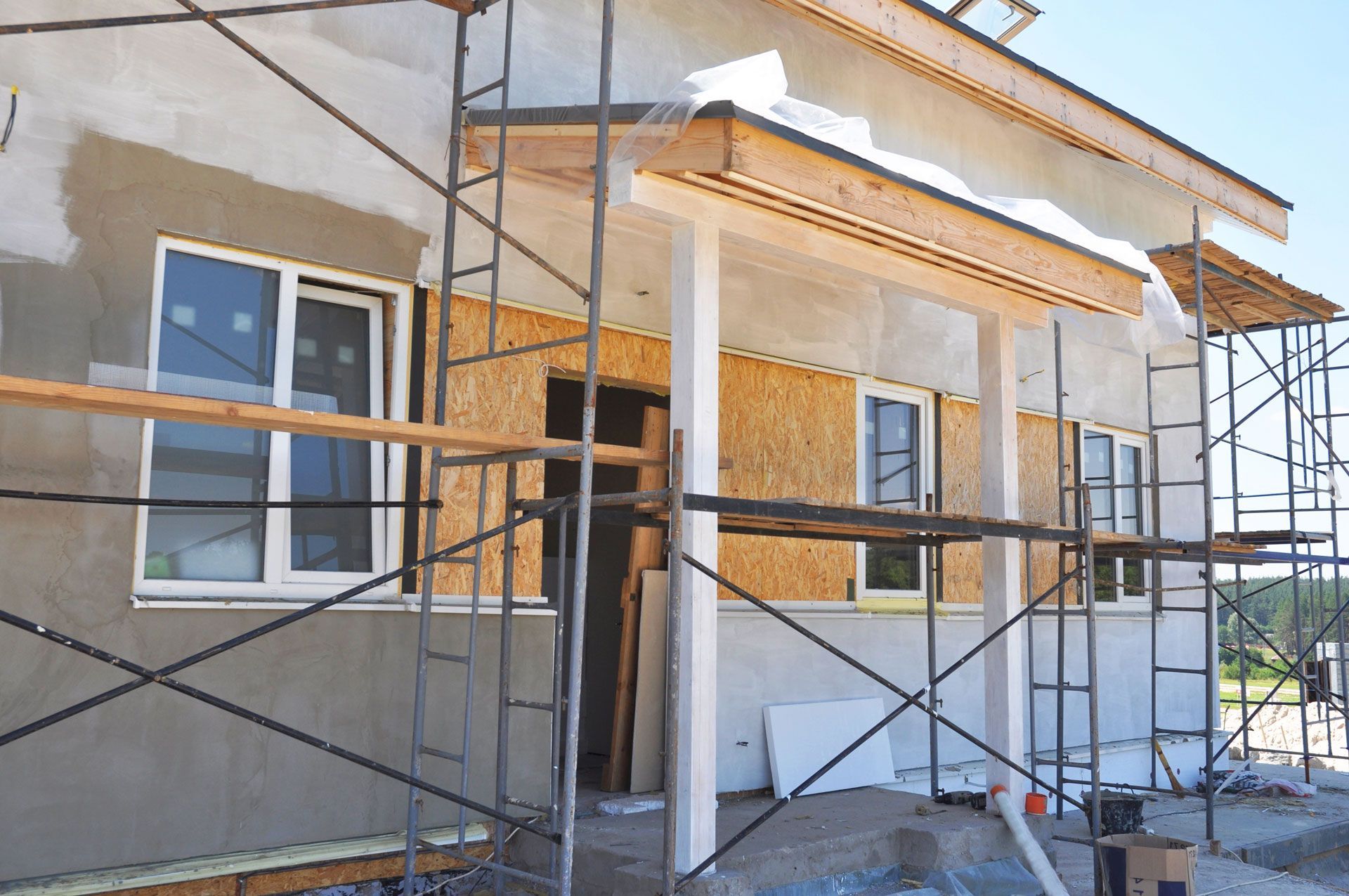 A house under construction with scaffolding around the exterior walls, exposed wood panels, and white window frames.