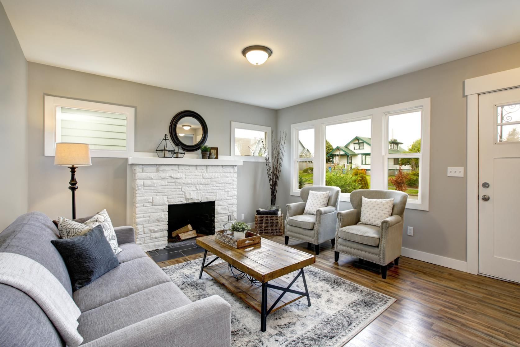 A modern living room with a grey sofa, fireplace, wooden coffee table, two armchairs, and a white entry door.
