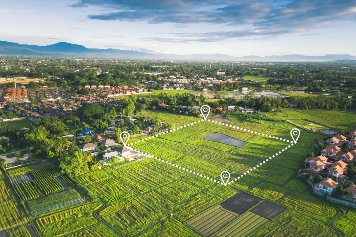 Aerial view of a green field marked with location pins, outlining a property plot within a suburban landscape.