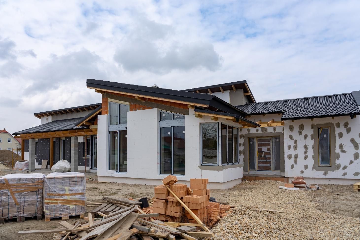 A modern, partially finished single-story home with a black sloped roof, white exterior walls, and piles of bricks outside.